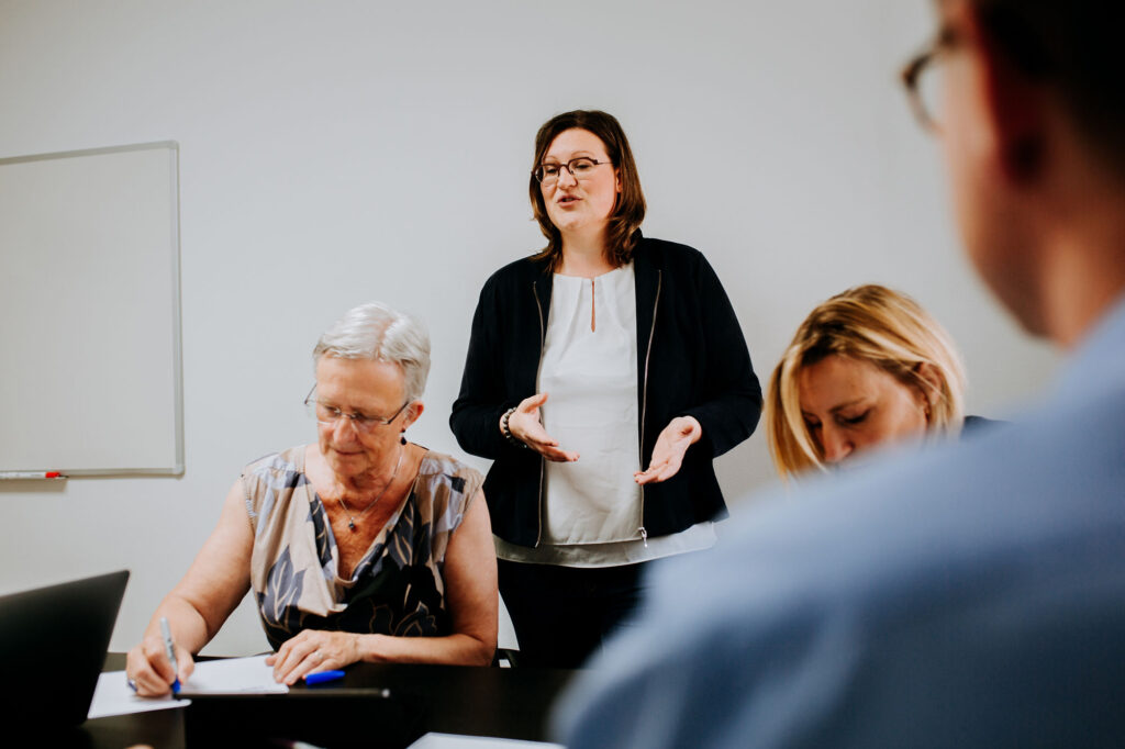 Communication trainer Ellen Bracquine standing and explaining to three clients seated around the table